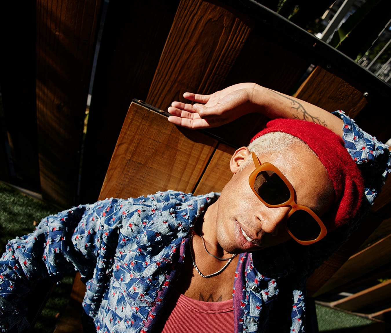 A man in sunglasses, a red beanie and a printed denim jacket